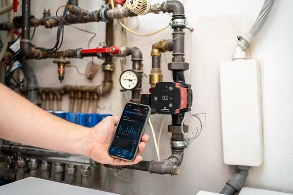 Bomba circuladora ALPHA2 GO instalada en tubería con smartphone mostrando la app Grundfos GO en tiempo real